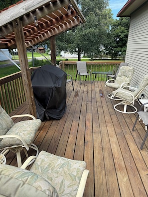 A wooden deck with outdoor furniture, including chairs and a covered grill area.
