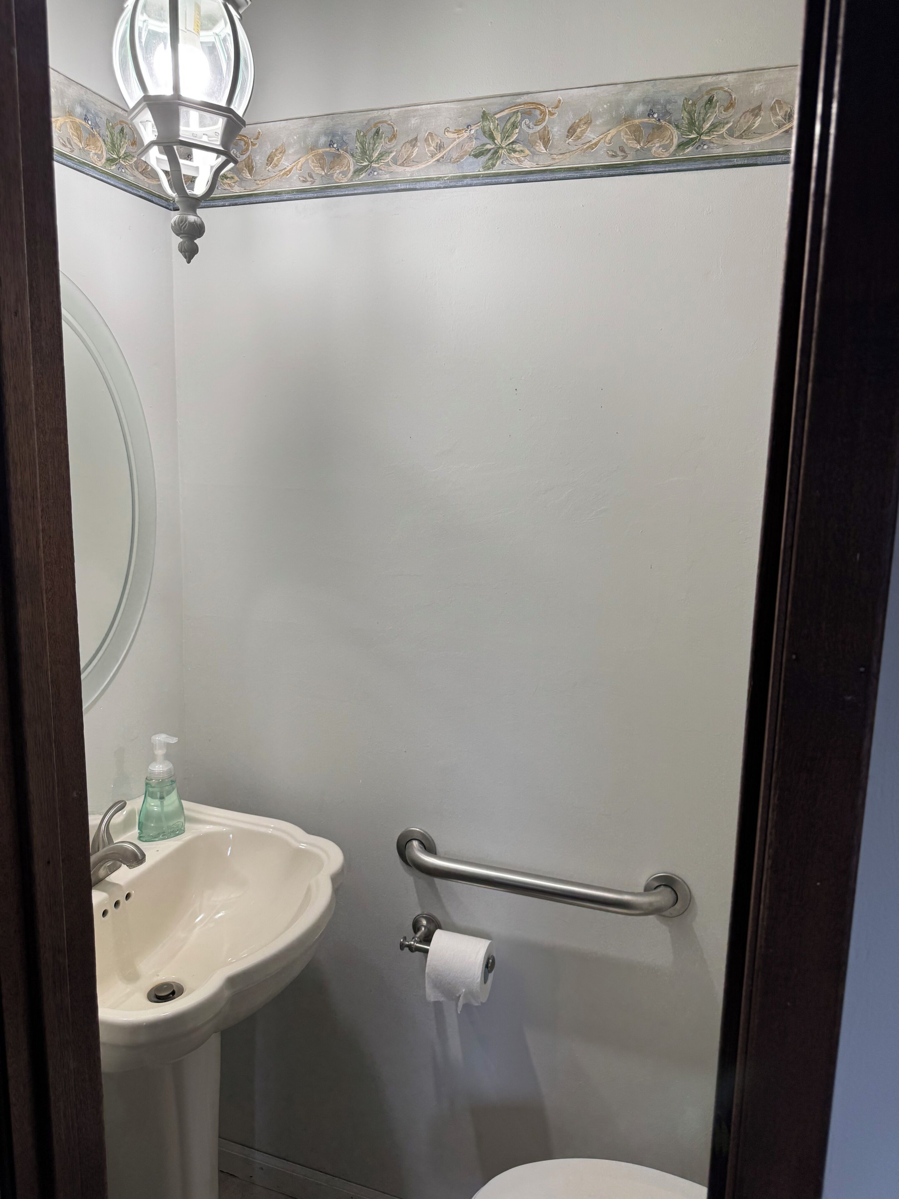 A bathroom with a pedestal sink, a toilet, a handrail, and a mirror.