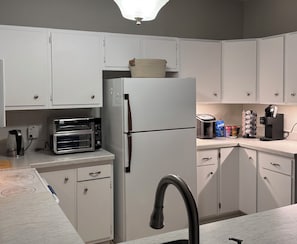 A kitchen with white cabinets, a built-in toaster oven, a refrigerator, and a coffee maker on the countertop.