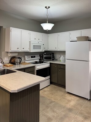 A modern kitchen with white cabinets, a microwave, a toaster oven, a refrigerator, and a sink.