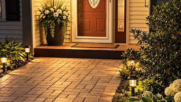 A house entrance with a wooden door, a potted plant, and a brick pathway.