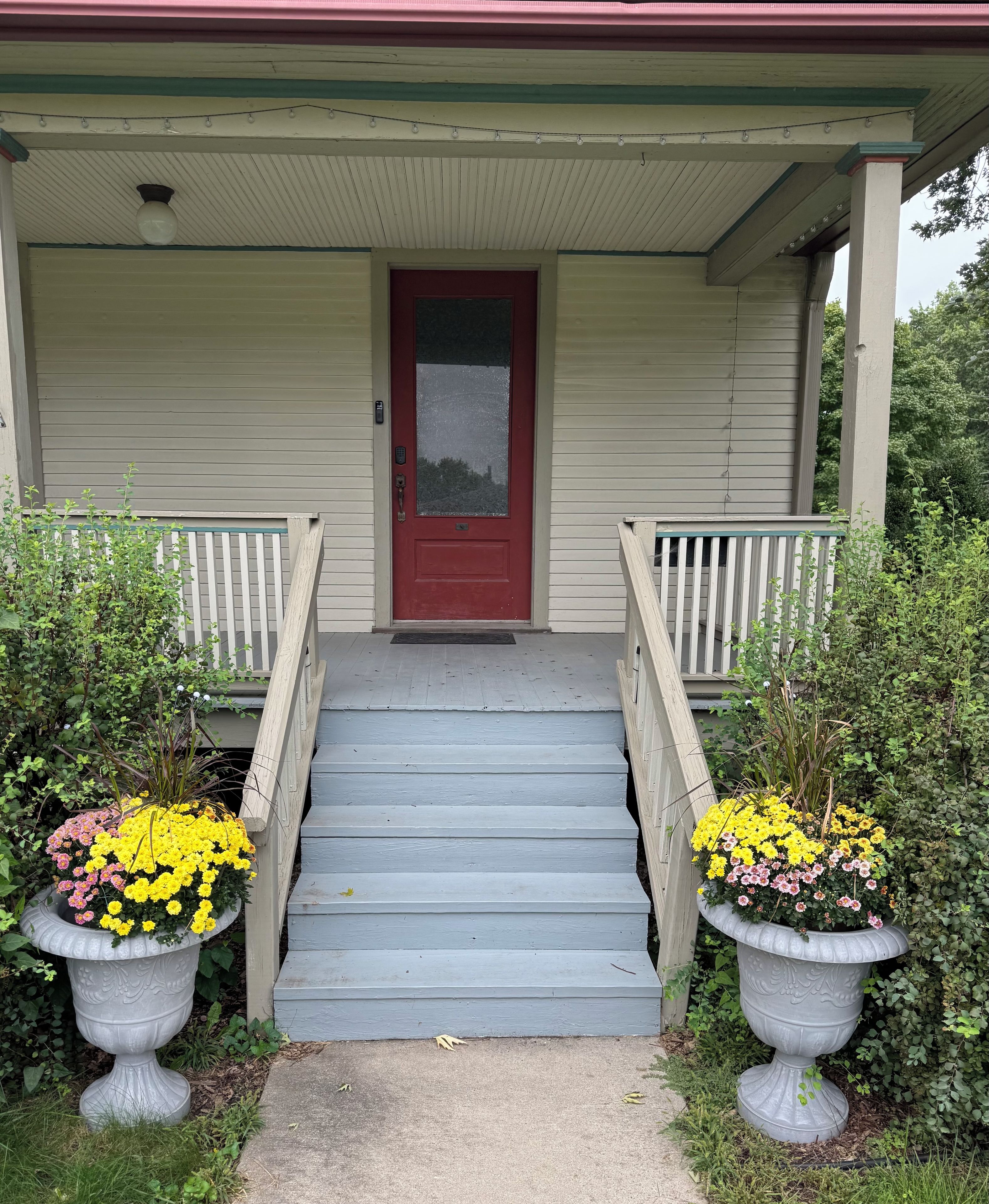 A porch with a red door, wooden steps, and two large flower pots.