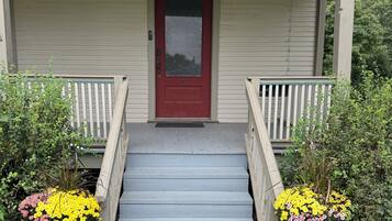A porch with a red door, wooden steps, and two large flower pots.