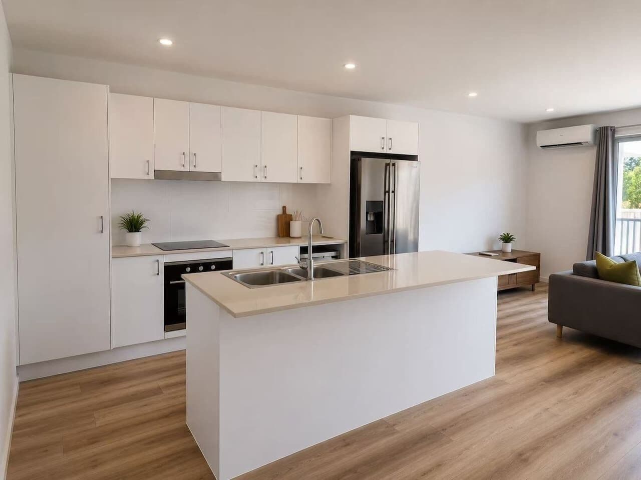 Een moderne keuken met witte kastjes, een centraal eiland met een spoelbak, een ingebouwde oven en een roestvrijstalen koelkast.