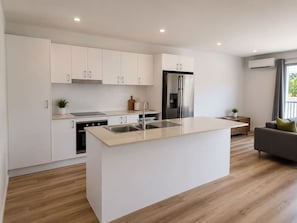 A modern kitchen with white cabinetry, a central island with a sink, a built-in oven, and a stainless steel refrigerator.