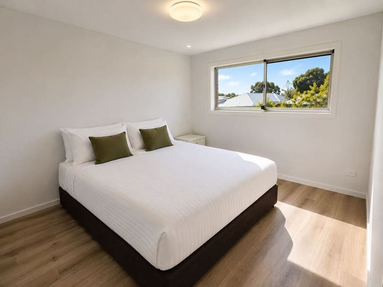 Quarto com cama grande, mesa de cabeceira, janela com vista e luminária de teto.