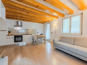 Eine moderne Küche mit Holzbalken, einem Essbereich mit Tisch und Stühlen sowie einer Couch in einem Wohnbereich.