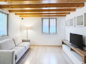 Un soggiorno moderno con un divano, una TV su un mobile in legno, una lampada da terra e una finestra con tende.
