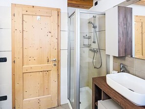 Un bagno con una porta in legno, uno spazio doccia in vetro e un lavandino bianco.