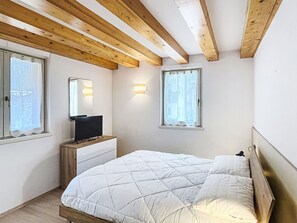 Una camera da letto con un letto, una cassettiera, una TV e due finestre.