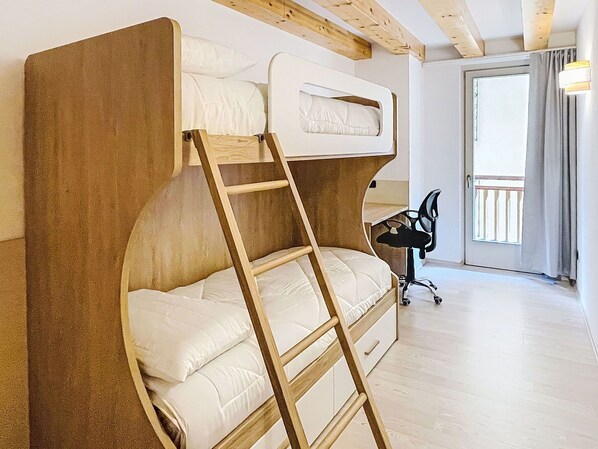 Un letto a castello con una scala, una scrivania e una sedia in una stanza con travi in legno e un'ampia finestra.