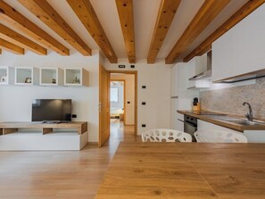 Eine moderne Küche mit Holzbalken, ein Essbereich mit Fernseher und ein Flur zu einem weiteren Zimmer.
