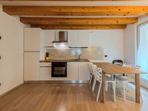 Een moderne keuken met houten balken, witte kasten, een inbouwoven en een eethoek met witte stoelen.