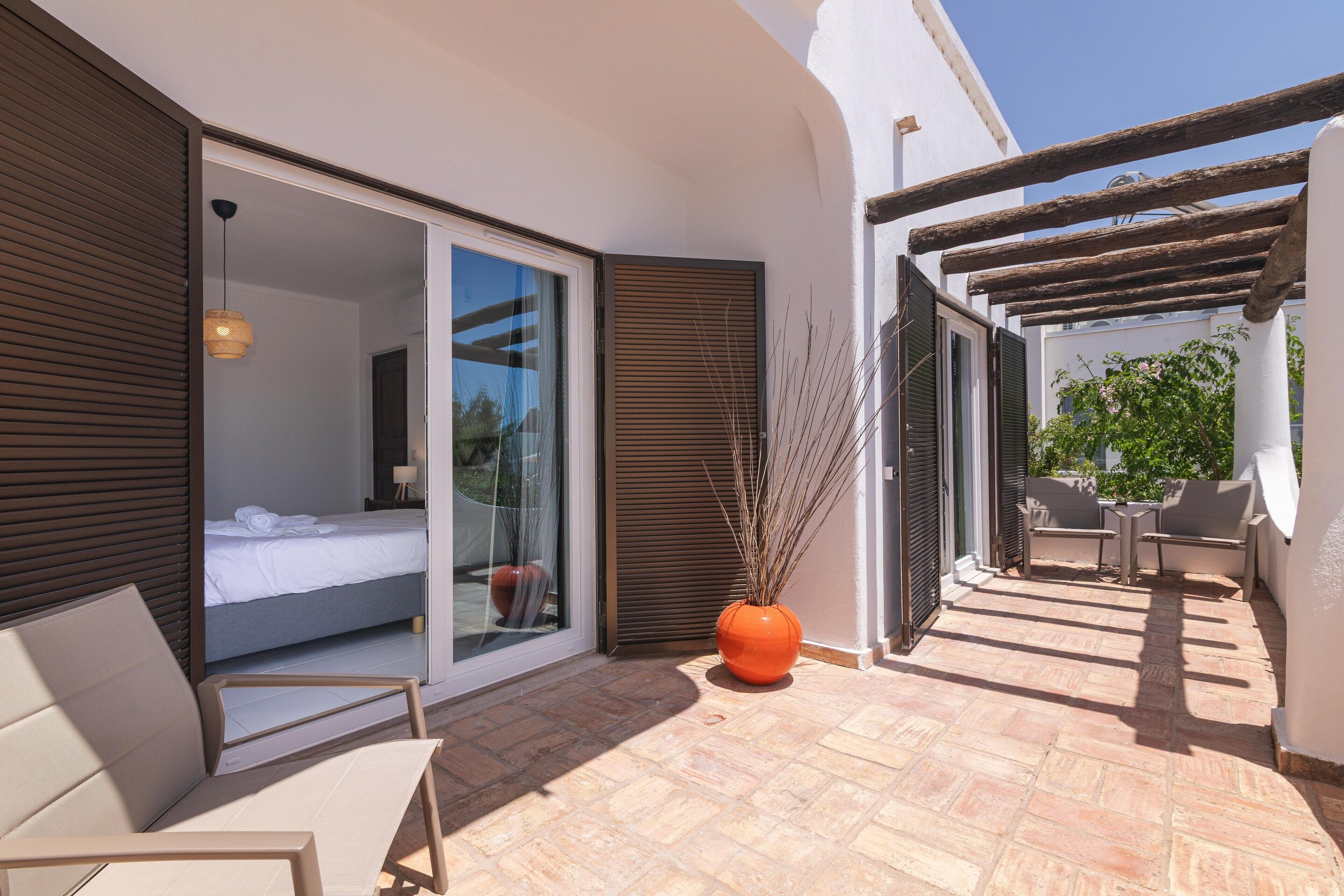 A modern outdoor patio with a bed, a seating area, and a large orange vase.