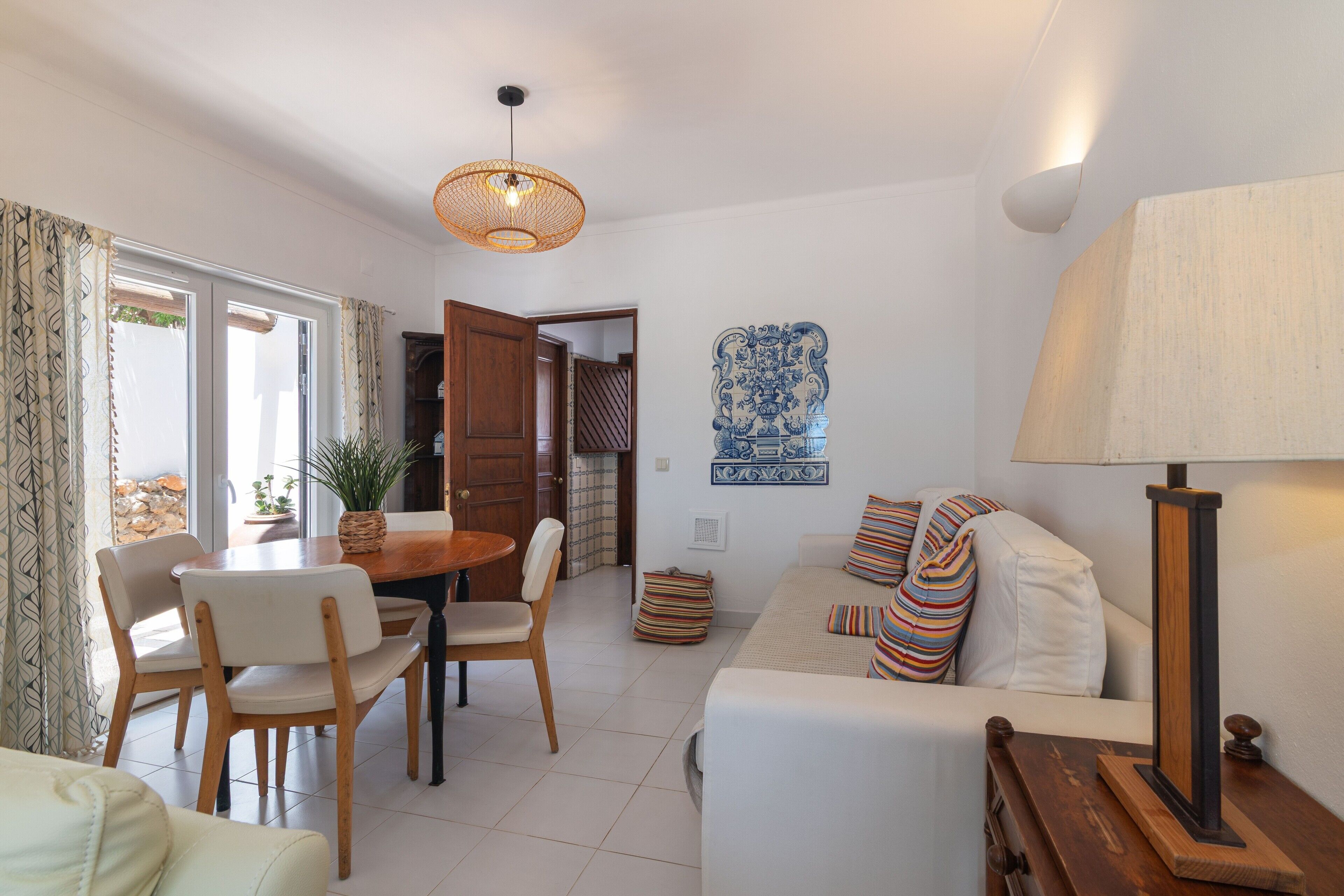 A living room with a sofa, a dining table with chairs, a hanging light fixture, and a wall-mounted decorative tile.