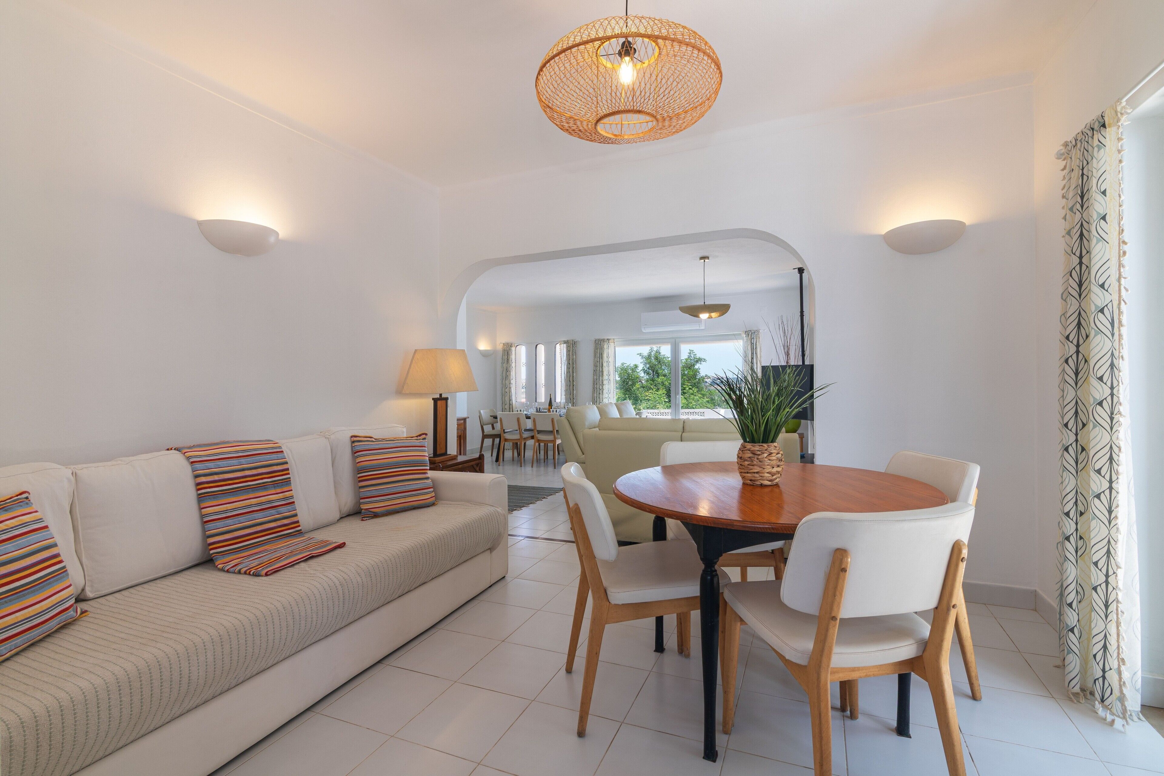 A modern living room with a sofa, a dining table with chairs, and a hanging light fixture.