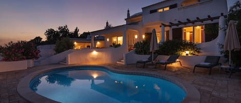 Eine moderne Villa mit Swimmingpool, Sitzgelegenheiten im Freien und einer gut beleuchteten Terrasse.