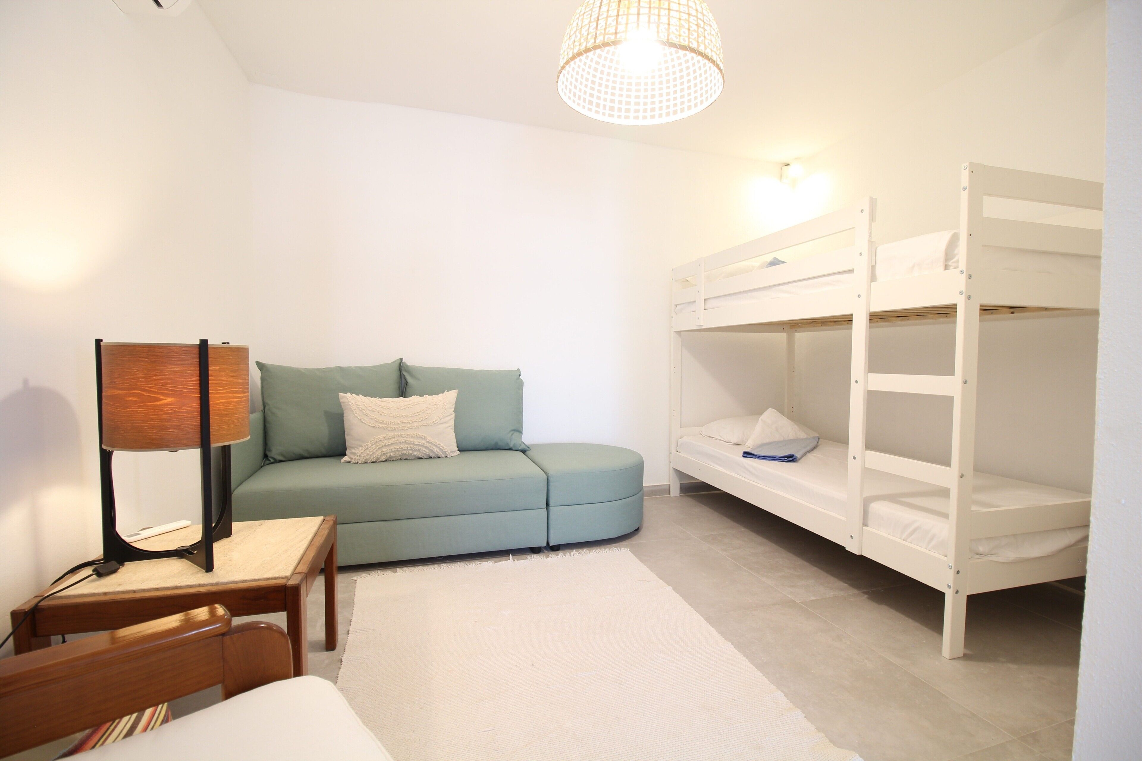 Ein Zimmer mit einem Etagenbett, einer Schlafcouch, einer Lampe und einem kleinen Tisch.