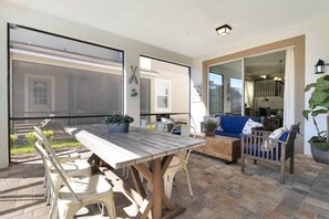 An outdoor patio with a wooden table and chairs, a blue sofa, and potted plants. - Exclusive 6 bedroom family vacation home! (Kissimmee)