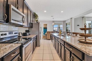 A modern kitchen with granite countertops, stainless steel appliances, and a large island. - Exclusive 6 bedroom family vacation home! (Kissimmee)