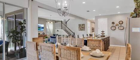 A modern kitchen with a dining area, featuring a chandelier, wicker furniture, and a refrigerator.