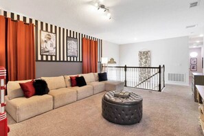 Un salon avec un canapé beige, un pouf rond et des rideaux à rayures.