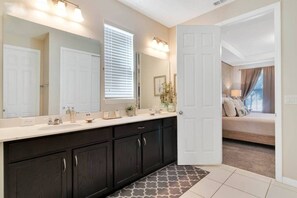 Une salle de bain dotée d’un grand miroir, de meubles sombres et d’une porte blanche donnant sur une chambre.