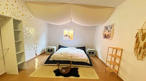 Ein Schlafzimmer mit einem Bett, einem Fenster, einem Nachttisch, einem Regal und einer Wanddekoration.