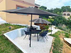 Eine Terrasse im Freien mit Tisch, Stühlen, einem Grill und einem großen Sonnenschirm.