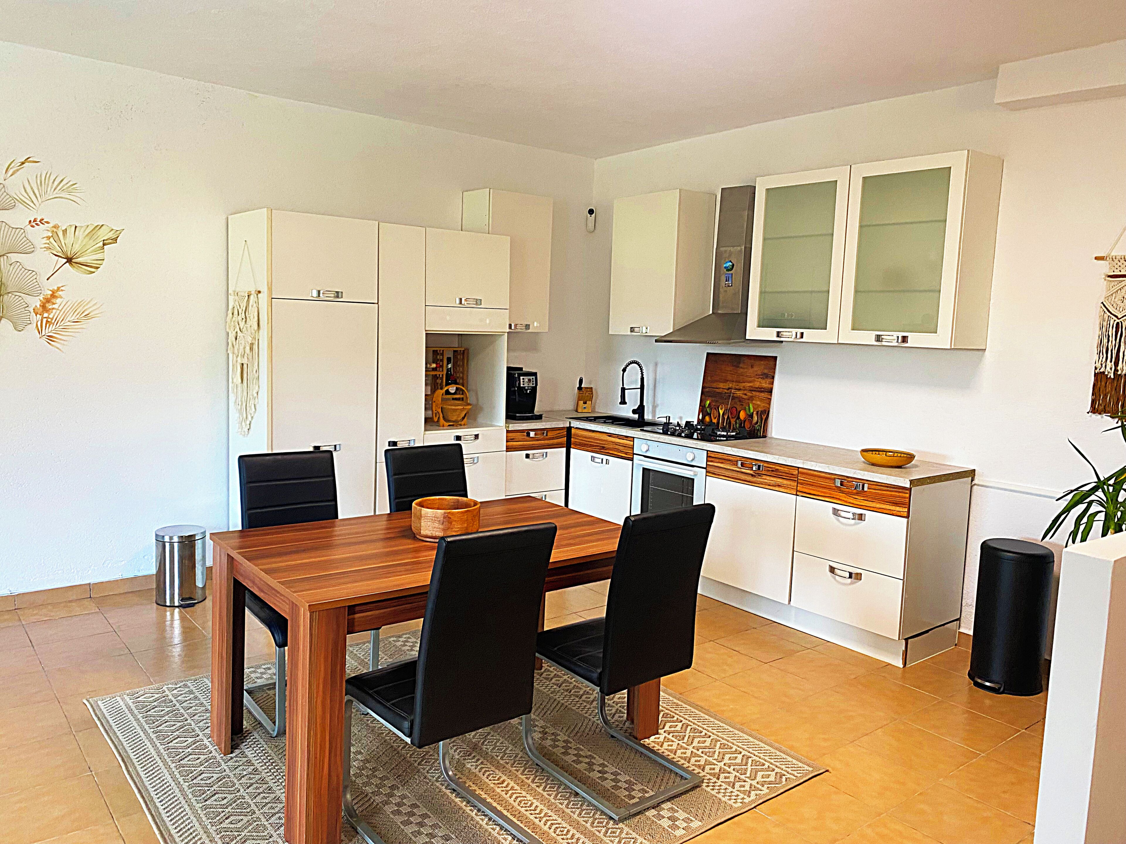 A compact kitchen with white cabinets, a wooden dining table, and black chairs.