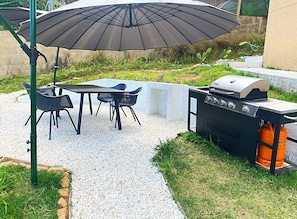 Eine Außenpatio mit Tisch und Stühlen, einem Grill und einem großen Sonnenschirm.