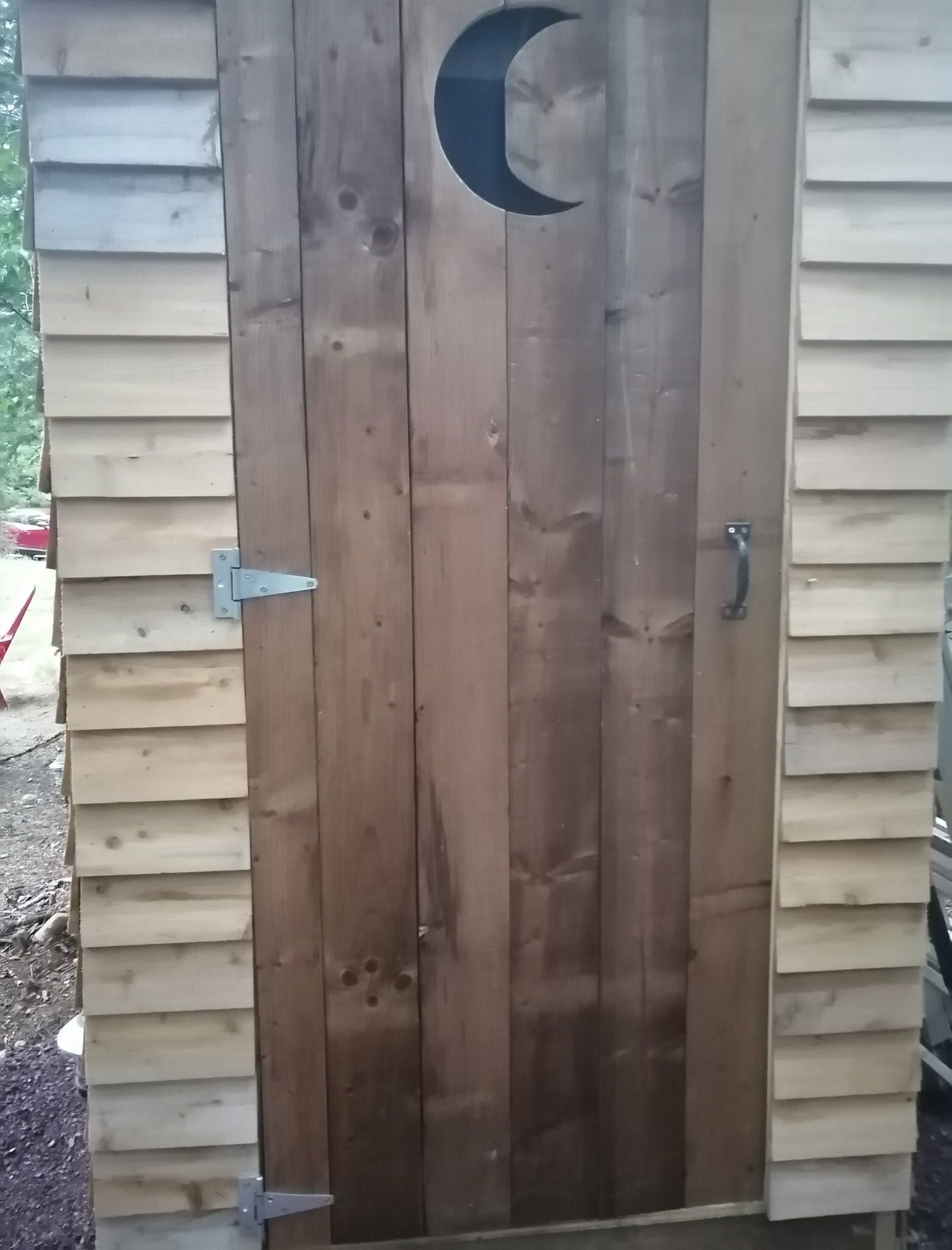 Une porte en bois ornée d’une découpe en forme de croissant de lune, d’un loquet métallique et d’un système de glissement pour l’ouverture.