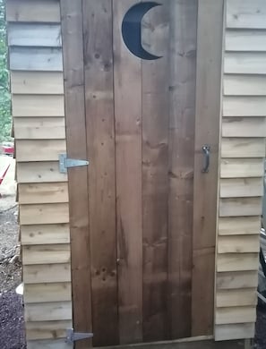 A wooden door with a crescent moon cutout, a metal latch, and a sliding door mechanism.