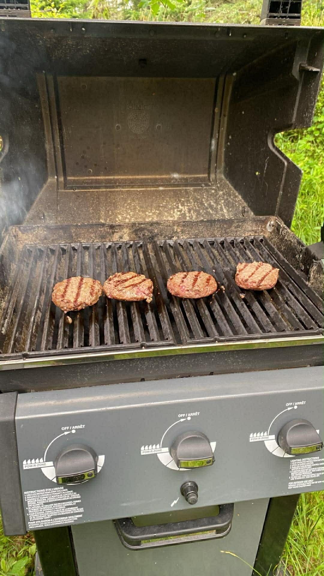 Un gril sur lequel sont en train de cuire trois hamburgers.
