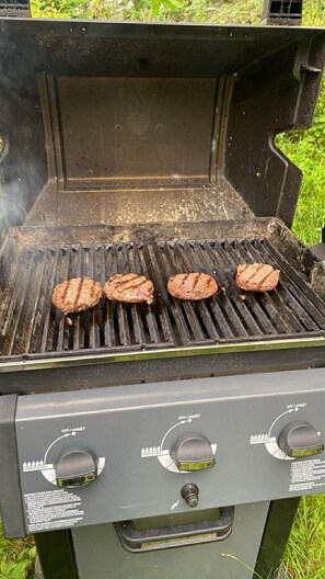 Een barbecue met daarboven drie burgers die worden gebakken.