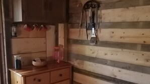 A wooden cabin interior with a wooden cabinet, a hanging tool, and a trash bin.