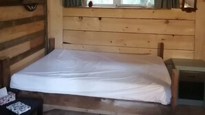 A cabin room with a bed, a small table, a window with curtains, and a welcome sign.