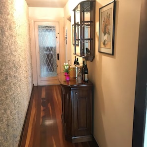 Ein Flur mit Holzboden, einer Tür mit dekorativem Glasfenster, einem Schrank mit Flaschen und einem gerahmten Bild an der Wand.
