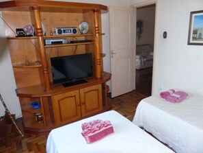Ein Zimmer mit einer Holz-Unterhaltungseinrichtung, einem Fernseher, einem Bett mit weißer Bettwäsche und einem pinkfarbenen Gegenstand auf dem Bett.
