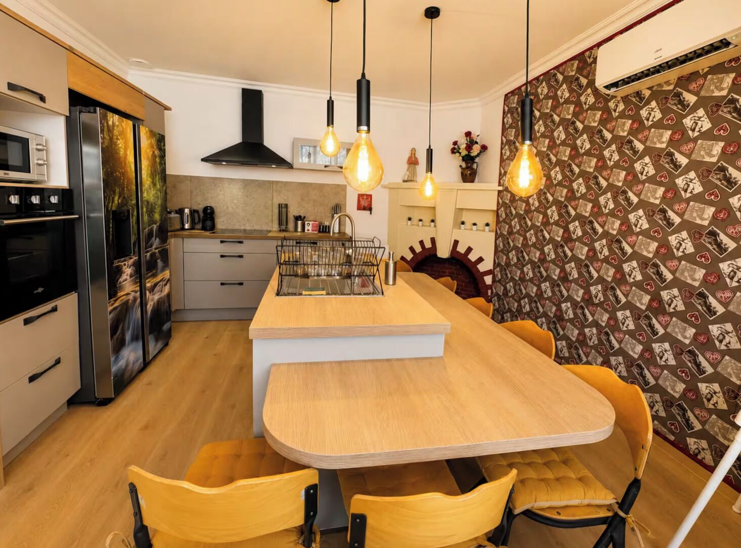 A modern kitchen with a central island, pendant lighting, and a patterned wallpaper.