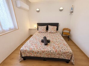 Ein Schlafzimmer mit floralem Bettbezug, einer Nachttischlampe, einem Sessel und einer Wand-Klimaanlage.