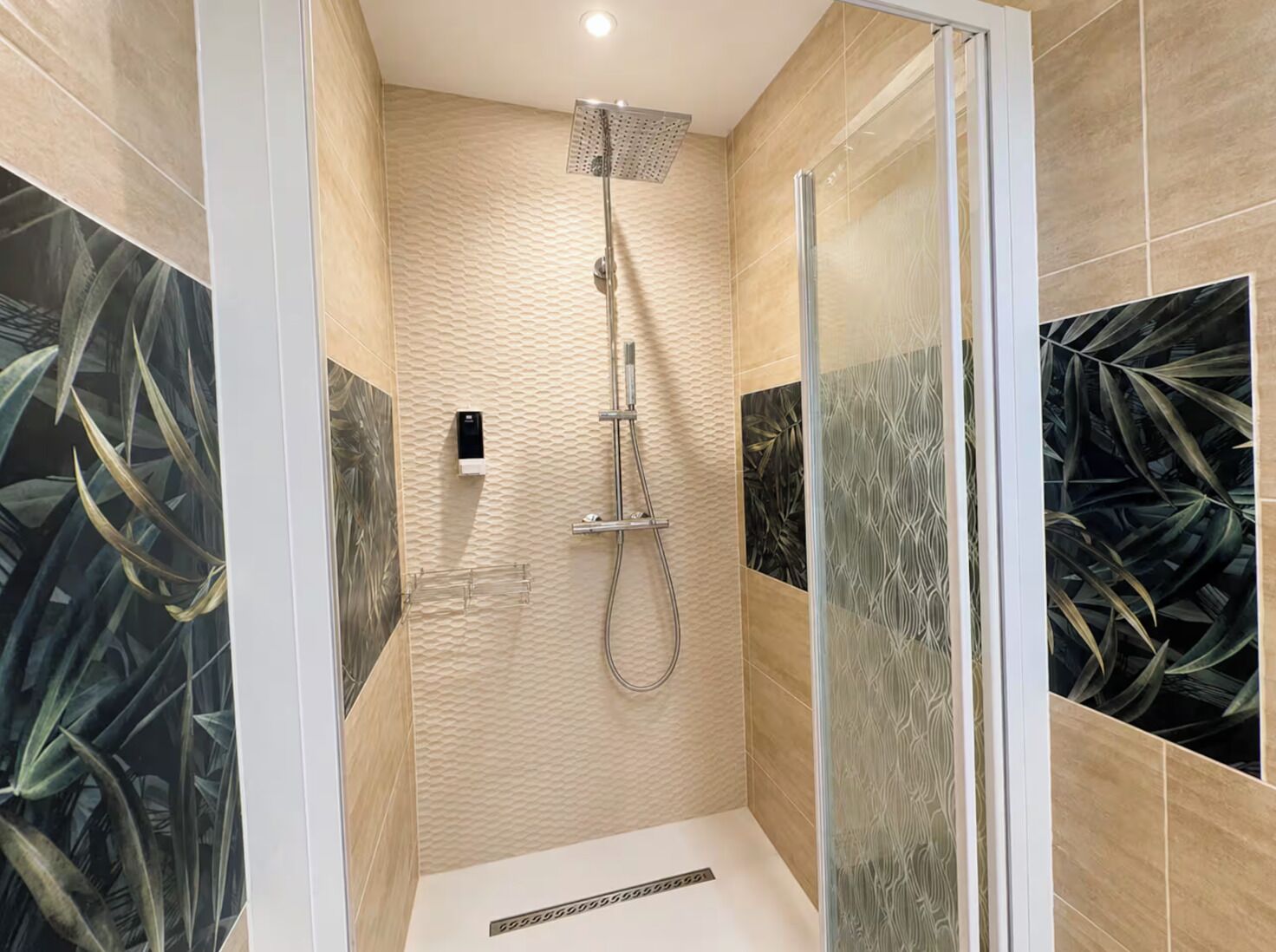 A modern shower with a glass door, a handheld showerhead, and a wall-mounted control panel.