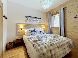 A bedroom with a wooden headboard, a bed with white bedding and fluffy throw, a wall-mounted artwork, and a window with curtains. - Santal - Les Gets - Selena Residence (Les Gets)
