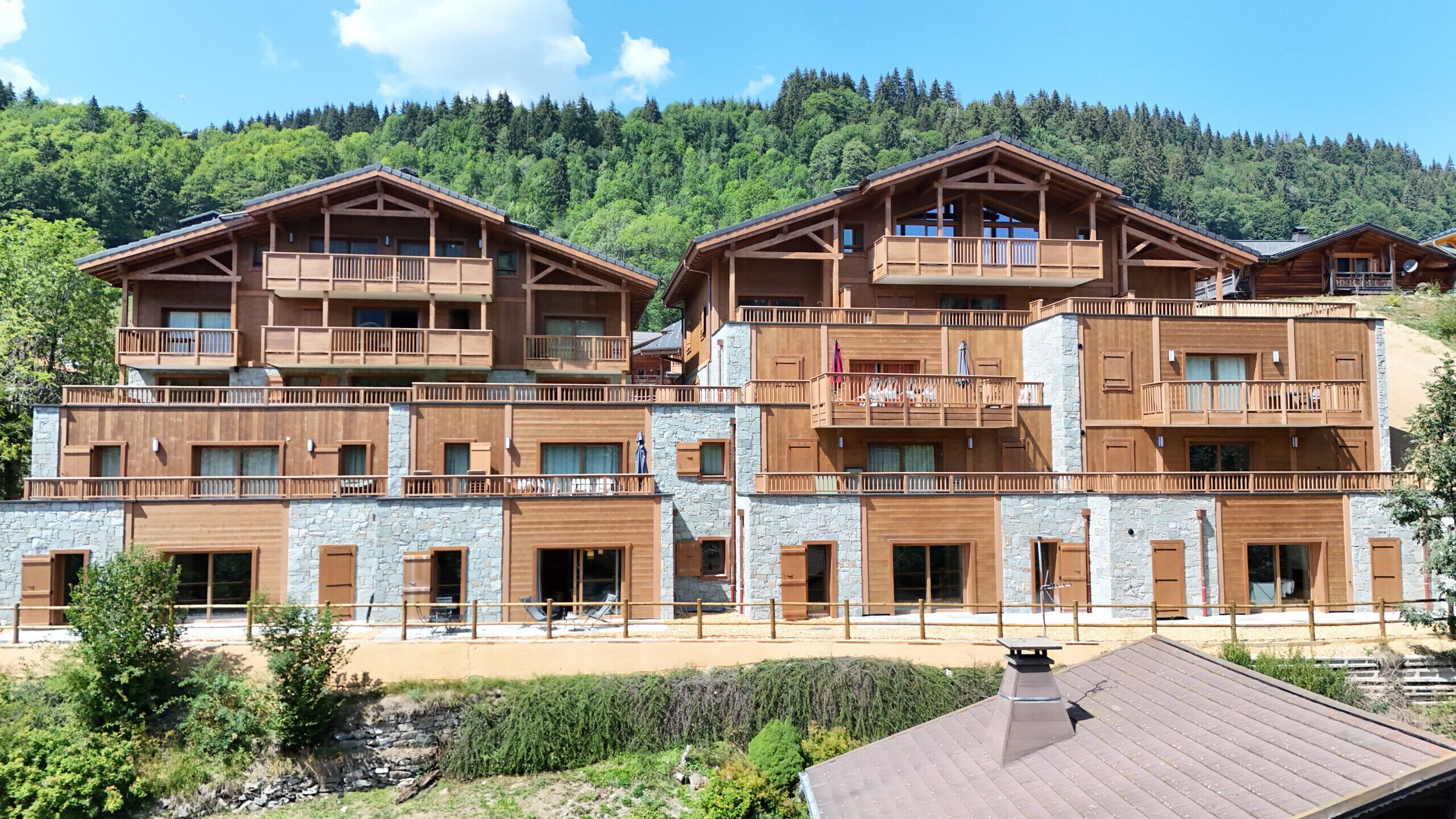 Un edificio de madera de varios pisos con balcones, detalles de piedra y vistas a una ladera boscosa.