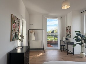 Una camera da letto moderna con pavimento in legno, un letto, una scrivania e un termosifone. Si vede un giardino dalla finestra.