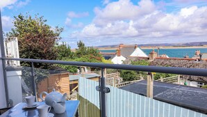 Ein Balkon mit einem für Tee gedeckten Tisch, mit Blick auf eine Küstenlandschaft mit Gebäuden und einem Gewässer.
