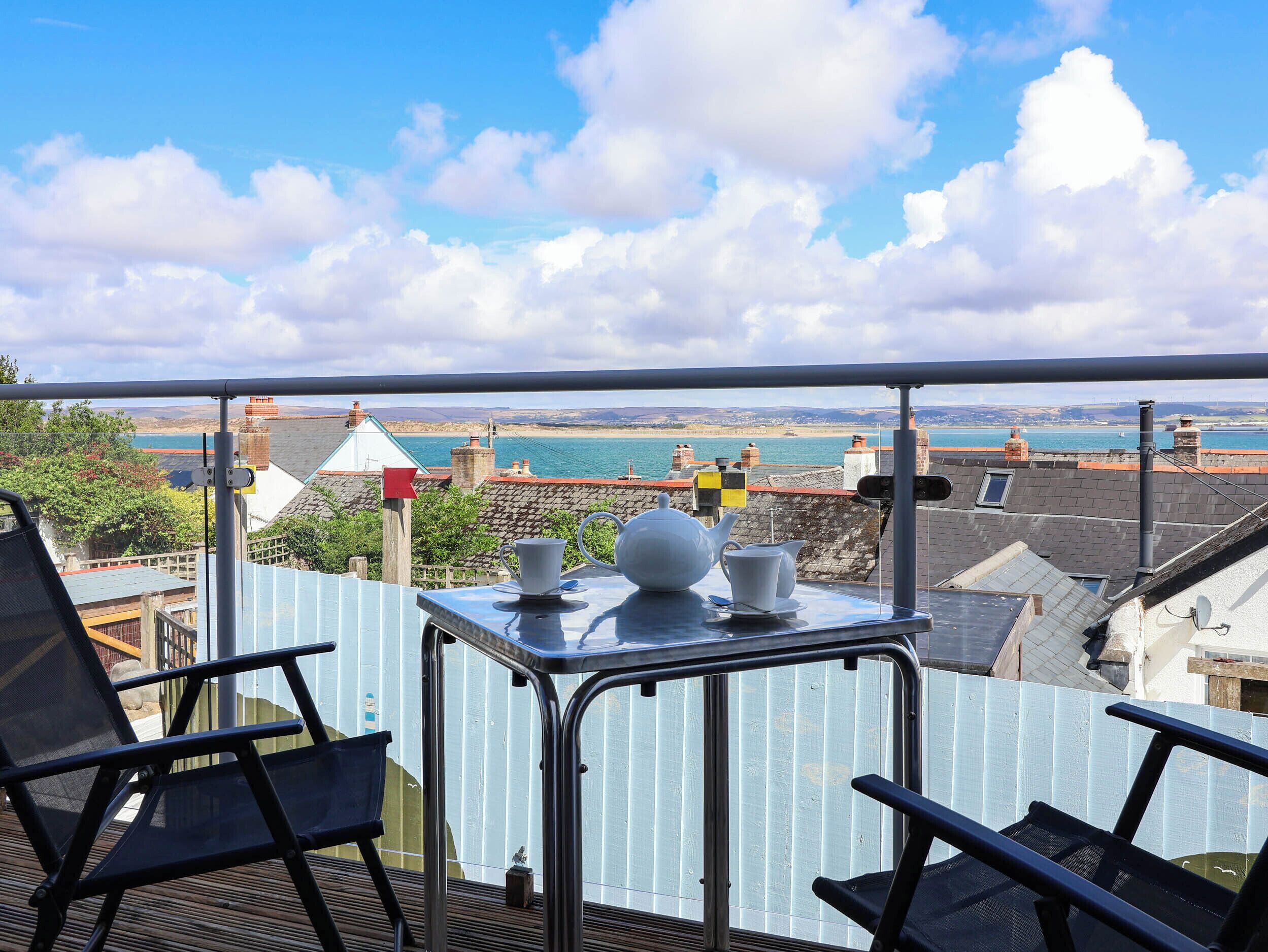A balcony with a table set for tea, overlooking a coastal view with buildings and a body of water.