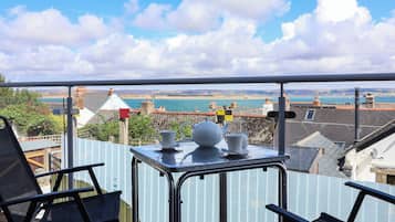 A balcony with a table set for tea, overlooking a coastal view with buildings and a body of water.