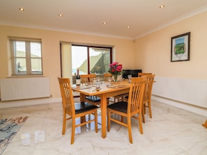 A dining area with a table set for six, wooden chairs, a vase with flowers, and a bottle of wine. - 1 Tideways (Bideford)