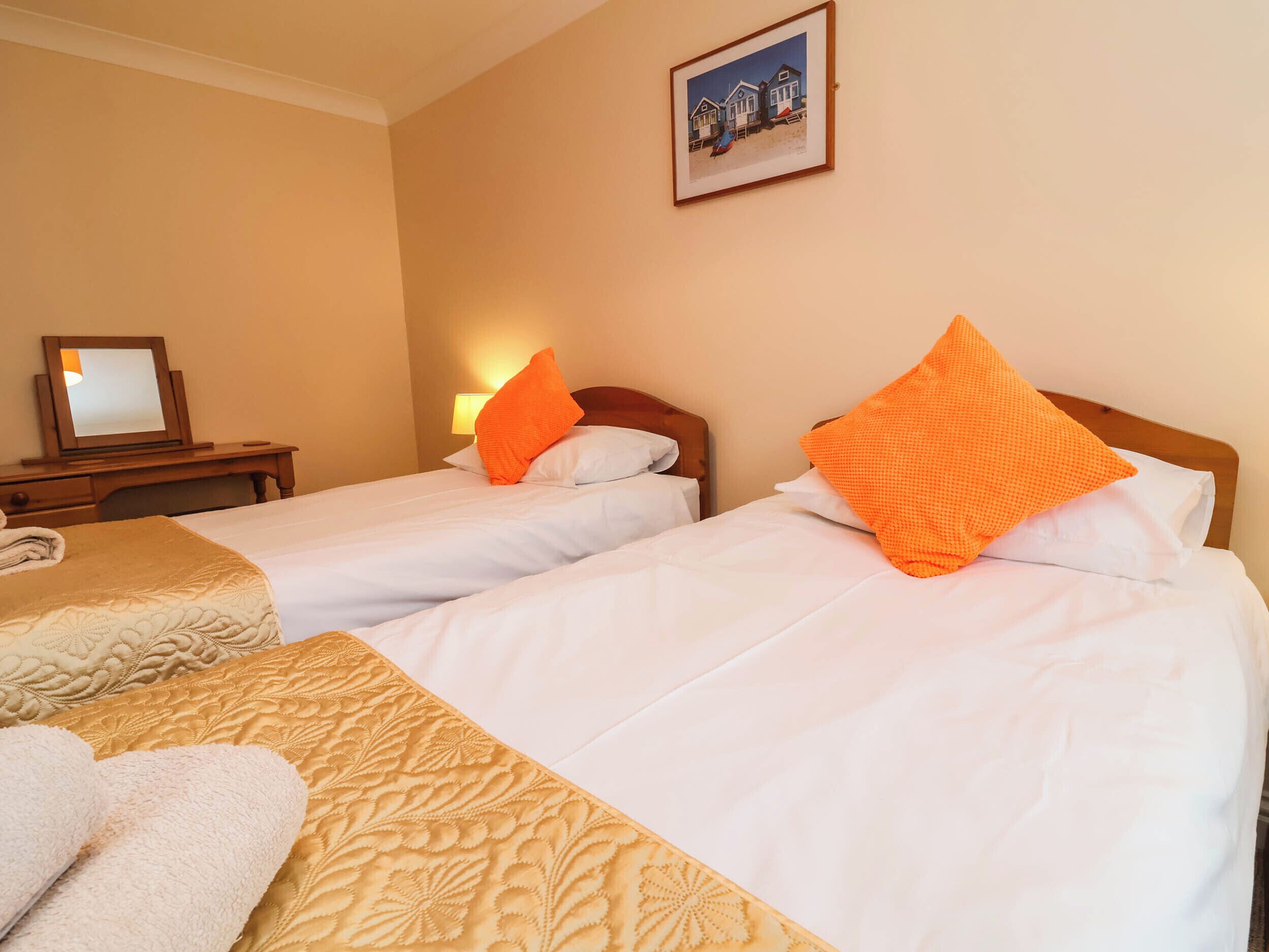 A hotel room with two beds, a bedside table, a lamp, and a framed picture on the wall.